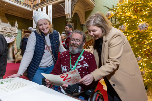 Three people wearing festive jumpers and winter clothing reading a piece of paper.