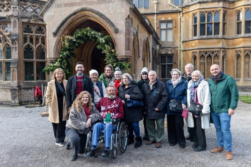 A group of people wearing winter clothing standing outside a Georgian manor home.