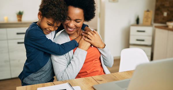 A child hugs their mother who sits at the kitchen table.