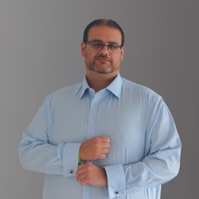 Lee, Customer Feedback Panel member, wearing a blue shirt, glasses stood against a grey backdrop.