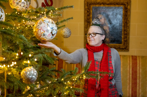 A lady wearing a bright red scarf looking at a large bauble on a Christmas tree.