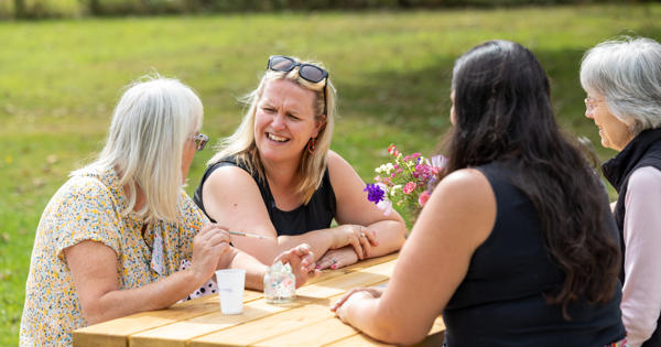 Four women sitting outside at a picnic bench talking