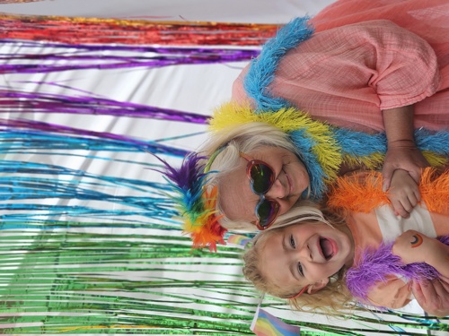 Grandmother and grandson wearing colourful rainbow accessories against a rainbow back drop.