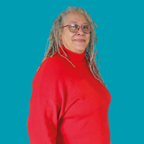 Yvonne, Customer Feedback Panel member, who has grey dreadlock-style hair, wearing glasses and a bright red turtle-neck jumper against a teal backdrop.